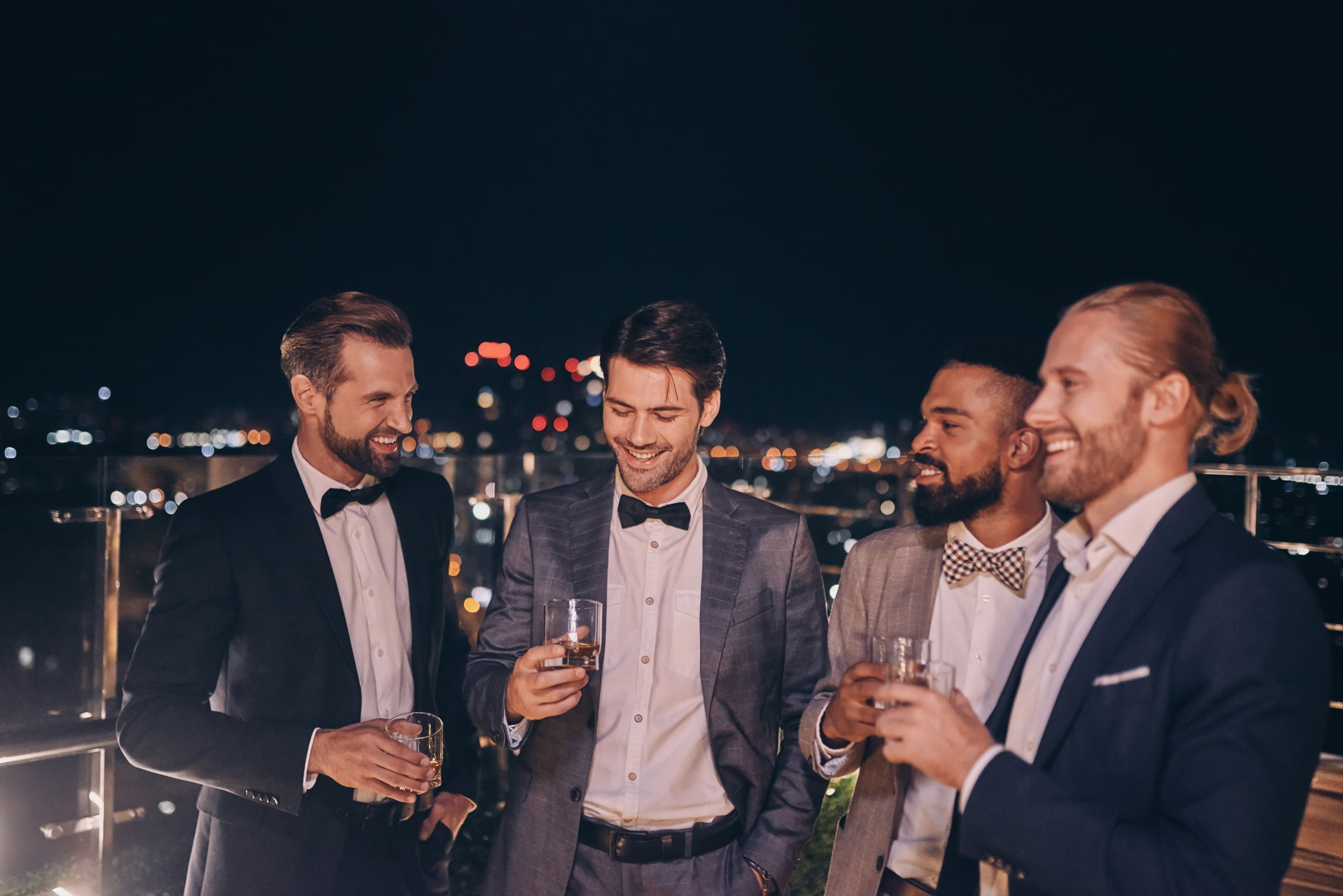 Group of handsome young men in suits and bowties drinking whiske